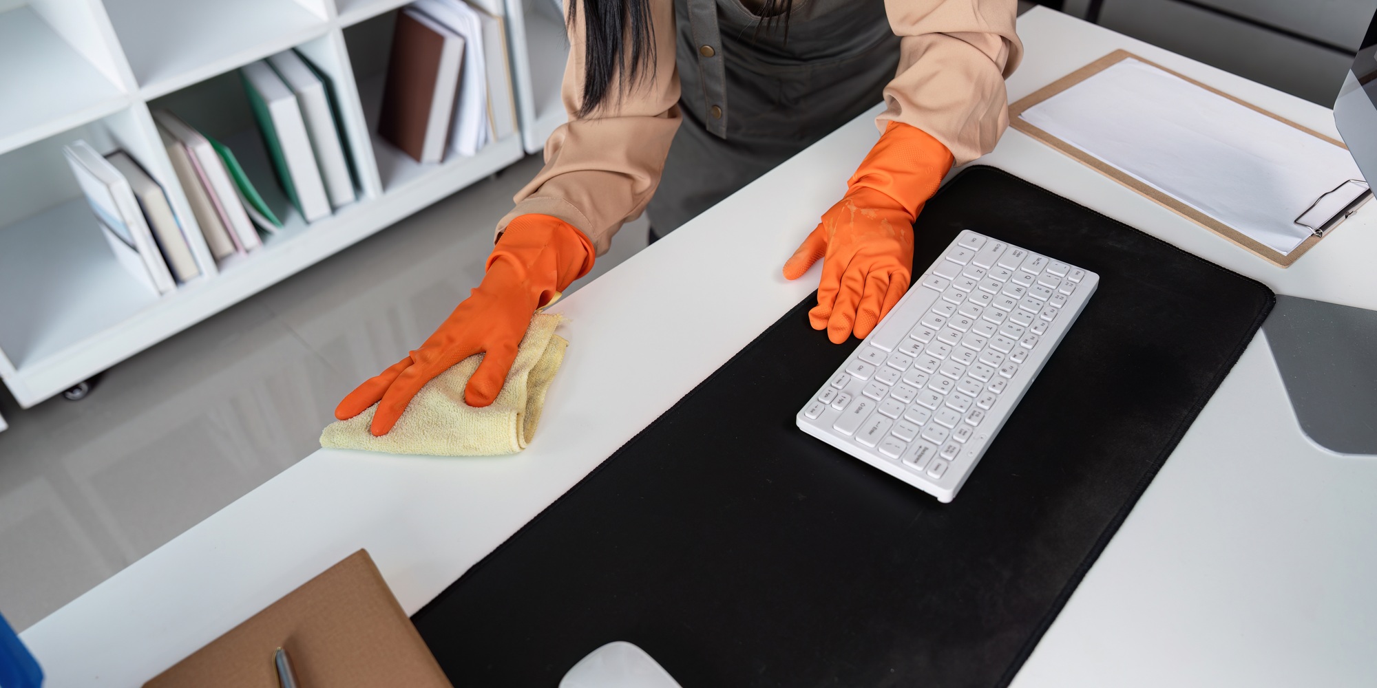Professional Maid Housekeeper Cleaning Office Desk with Orange Gloves and Cloth in Modern Workspace